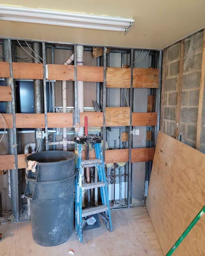 A room under construction with a ladder, buckets, and pipes