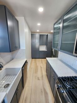 A long kitchen with gray cabinets, white counter tops, a stove and a sink