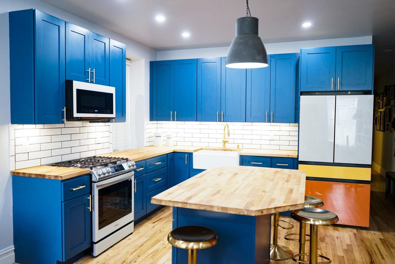 A kitchen with blue cabinets, wooden counter tops, stainless steel appliances, and a large island