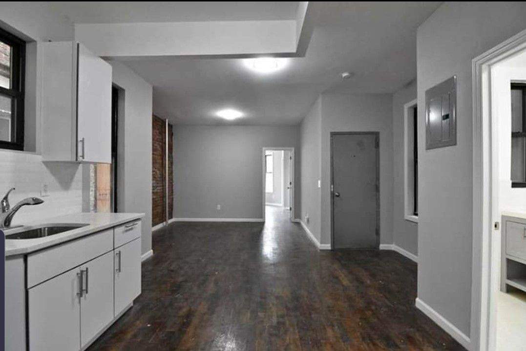 An empty apartment with hardwood floors and white cabinets