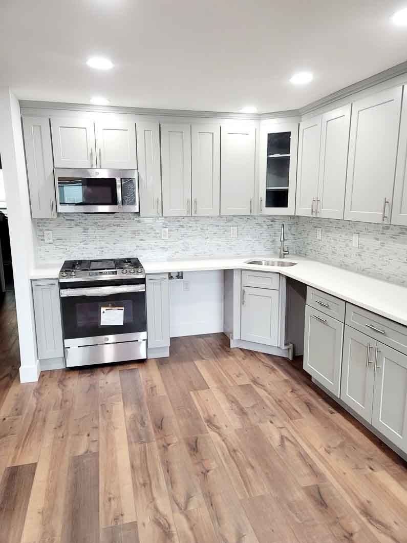 A kitchen with hardwood floors , white cabinets , a stove and a microwave