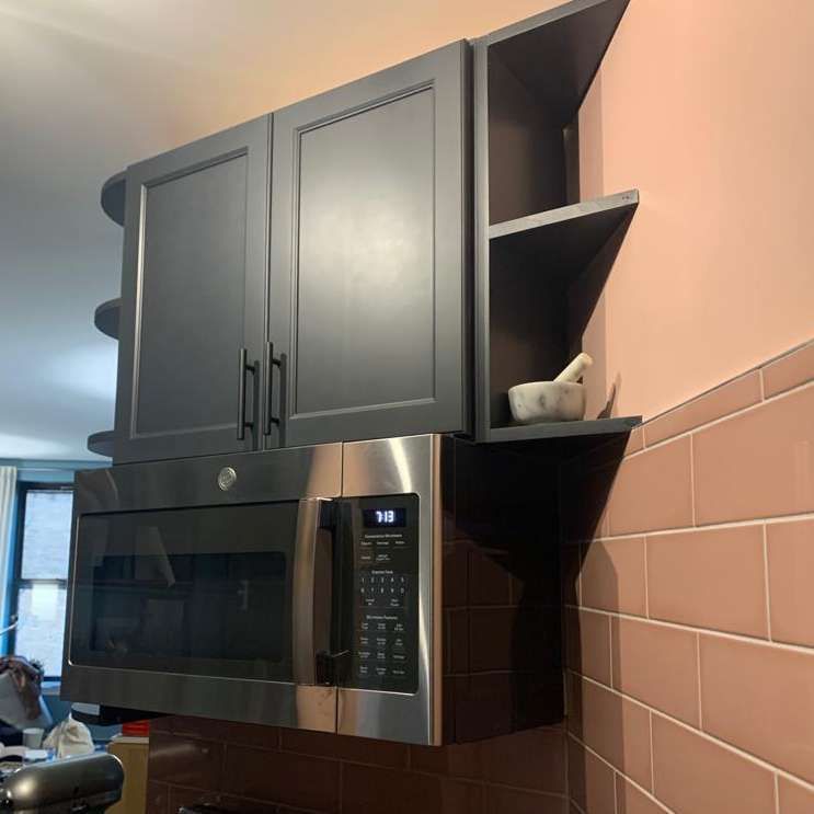 A kitchen with black cabinets and a stainless steel microwave