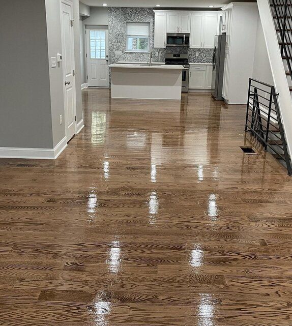 A living room with hardwood floors and a kitchen in the background