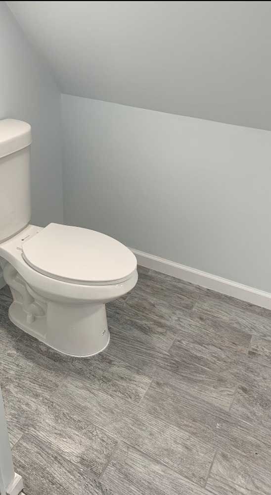 A white toilet is sitting on a wooden floor in a bathroom