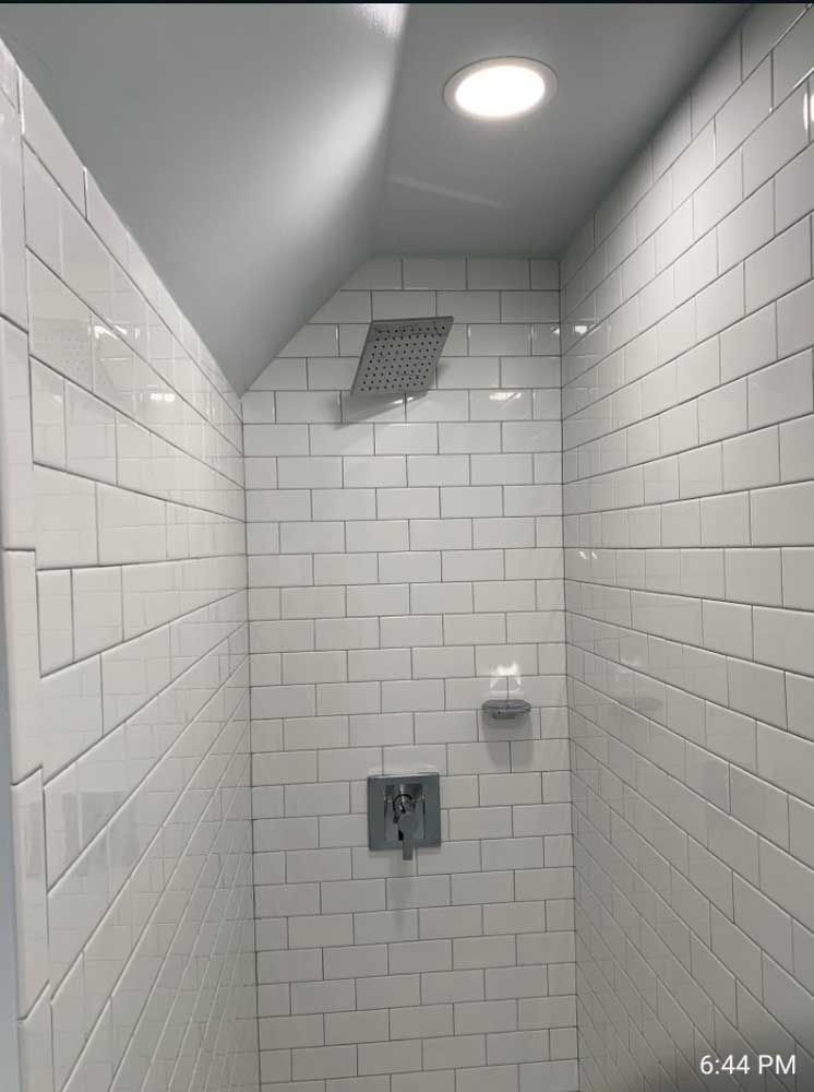 A shower with white tiles and a shower head