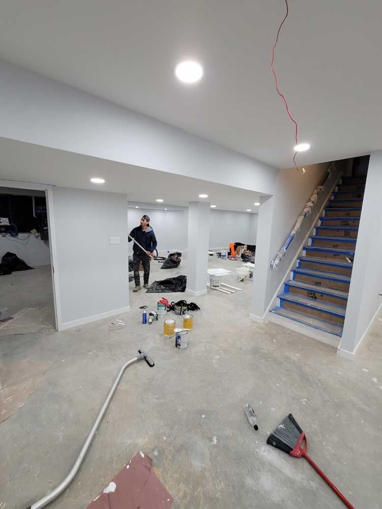 A man is vacuuming a basement with stairs in the background