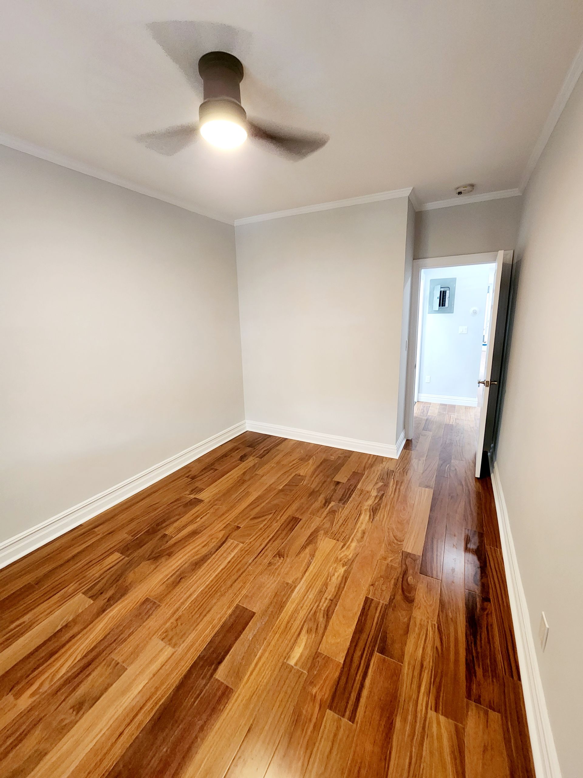 An empty bedroom with hardwood floors and a ceiling fan