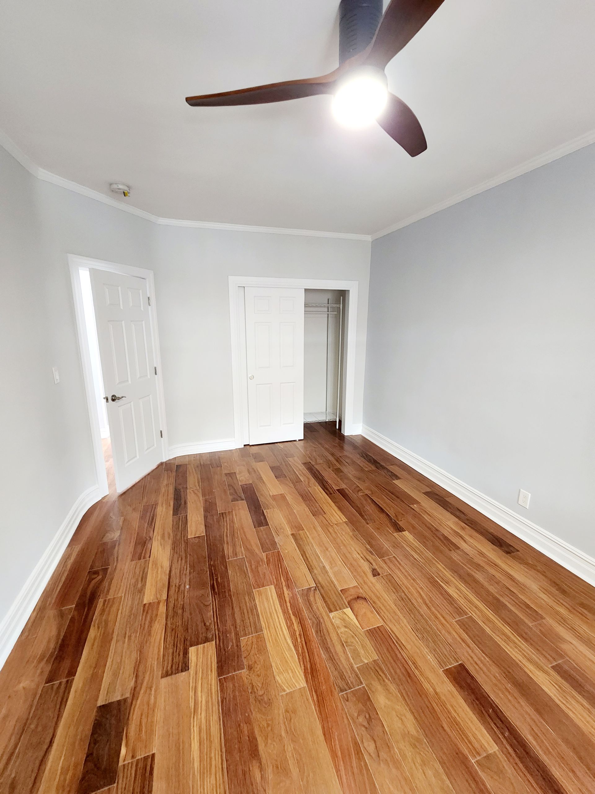 A bedroom with hardwood floors and a ceiling fan