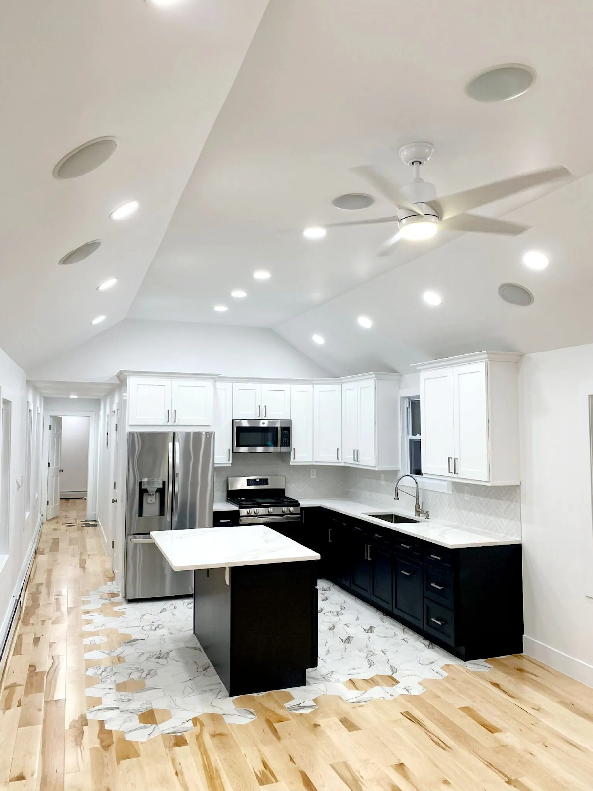 A modern kitchen features white upper cabinets, black lower cabinets, a stainless steel refrigerator, and a small island.