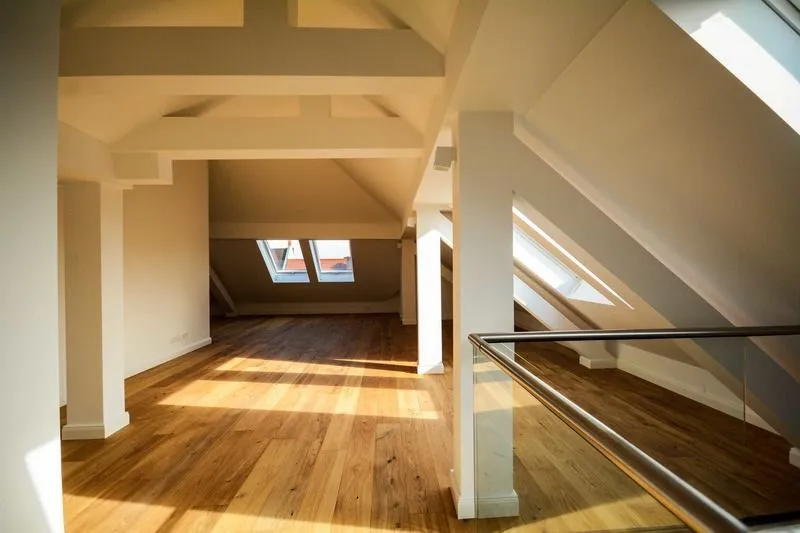 An attic space featuring light hardwood floors, white wooden support beams, and slanted ceilings with skylights.