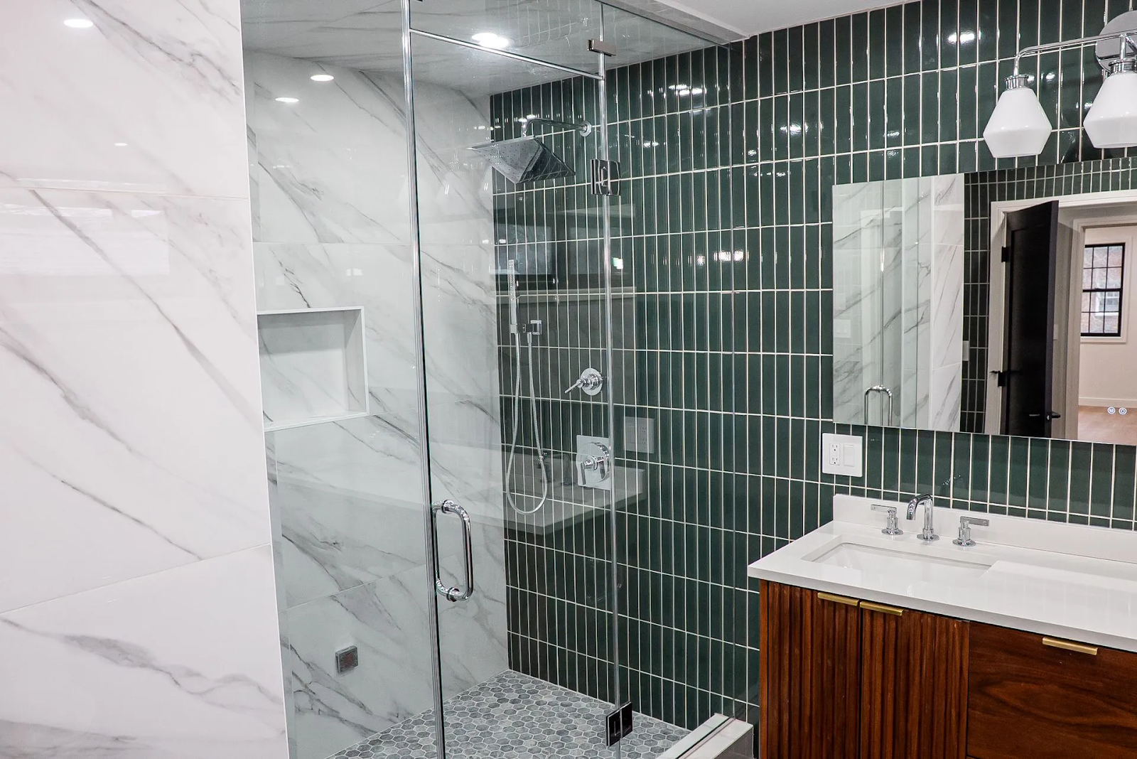 A modern bathroom with a glass-enclosed shower, white marble tile walls, a green vertical tile accent wall, and wood vanity.