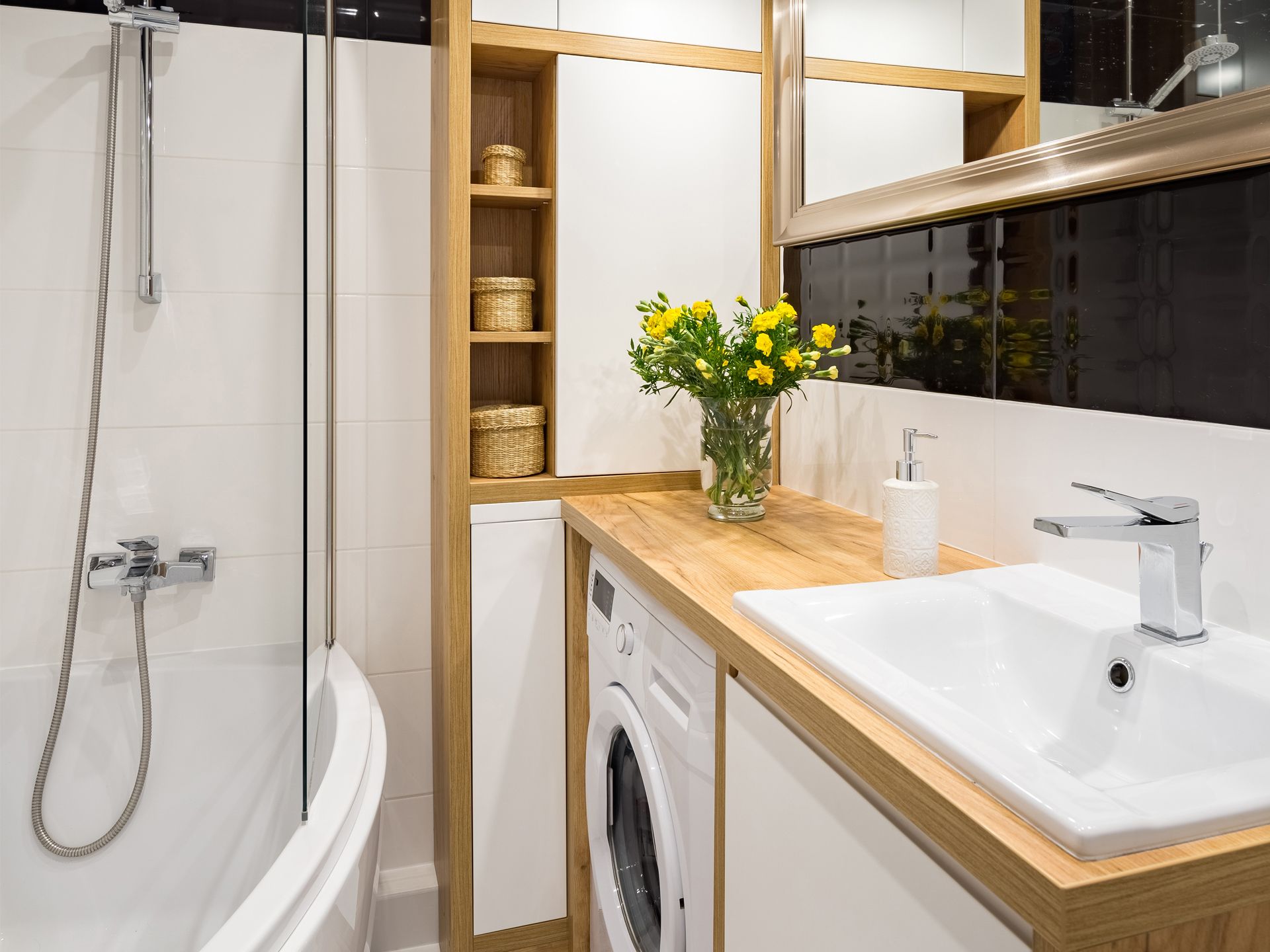 A small bathroom with a sink, washing machine, and shower