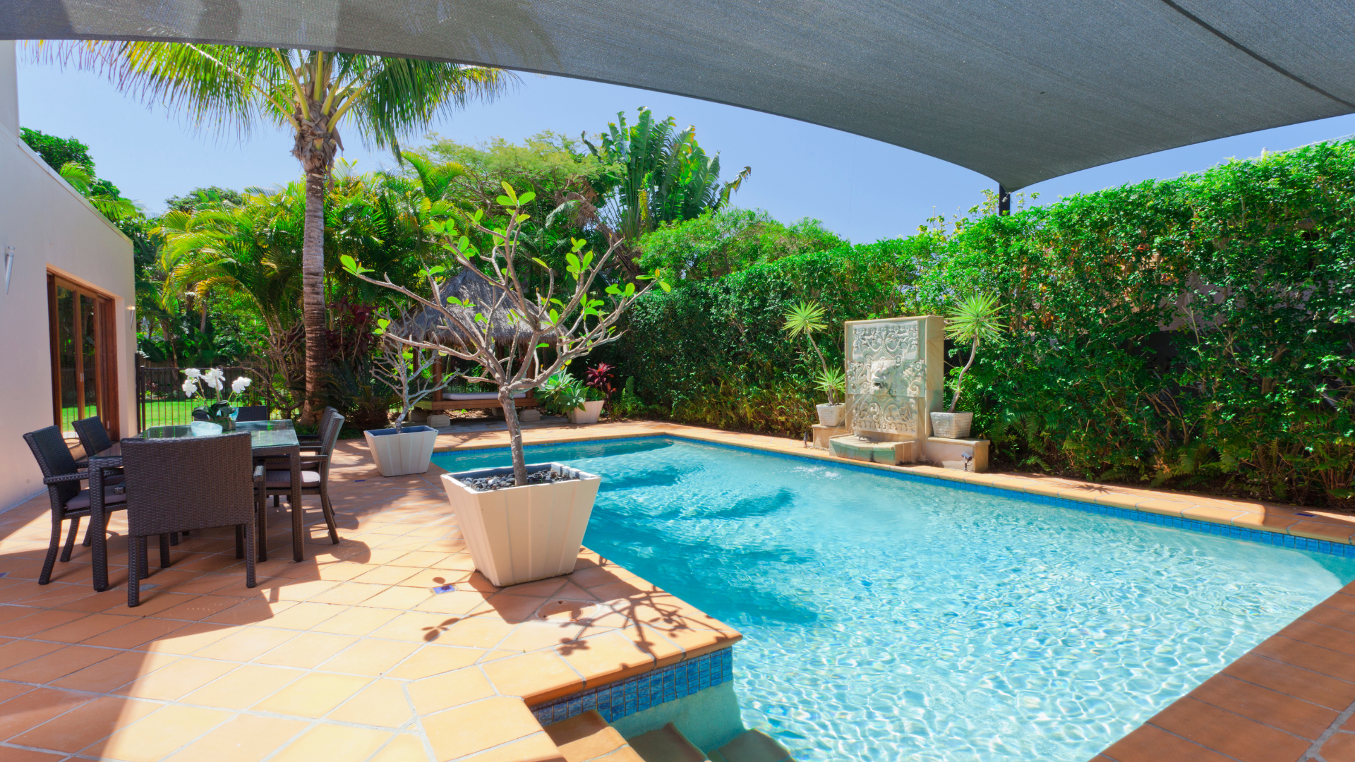 Metal pool ladder leading into a bright blue swimming pool with steam rising from the water in a backyard setting.