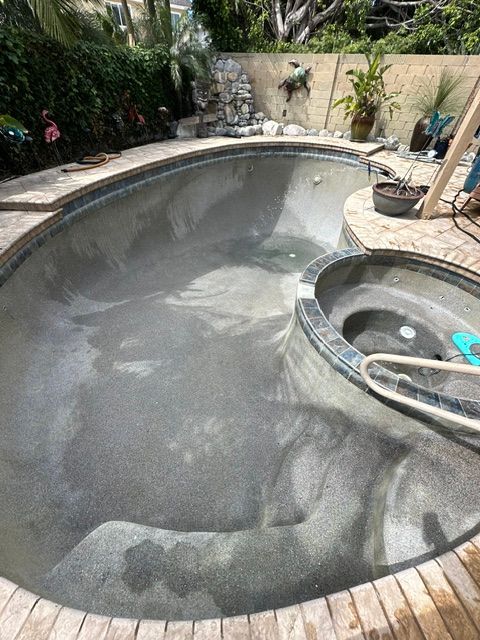 Empty backyard swimming pool being cleaned, with a dark wet surface and a hot tub beside it.