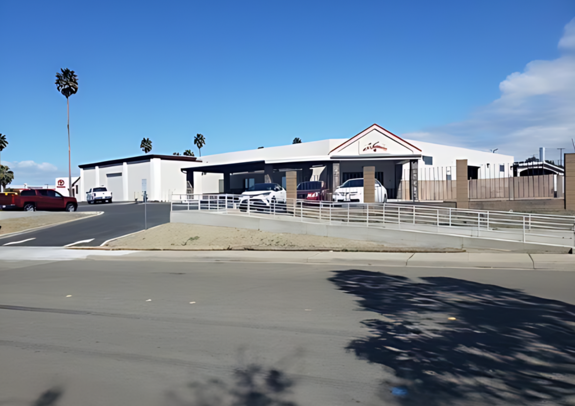 Building with cars parked in front, palm trees, and a blue sky.