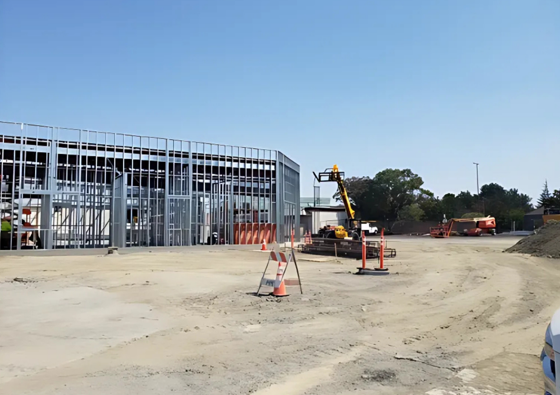 Construction site with metal framing, equipment, and dirt, under a blue sky.