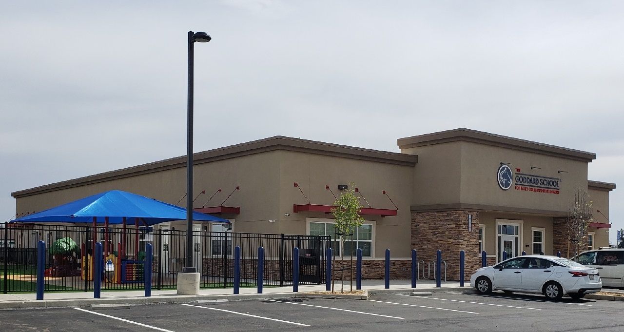 A white car is parked in front of a building with a blue umbrella.