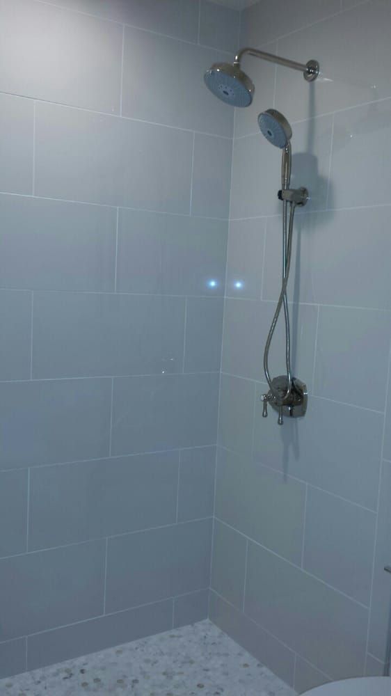 A shower with two shower heads and a toilet in a bathroom.