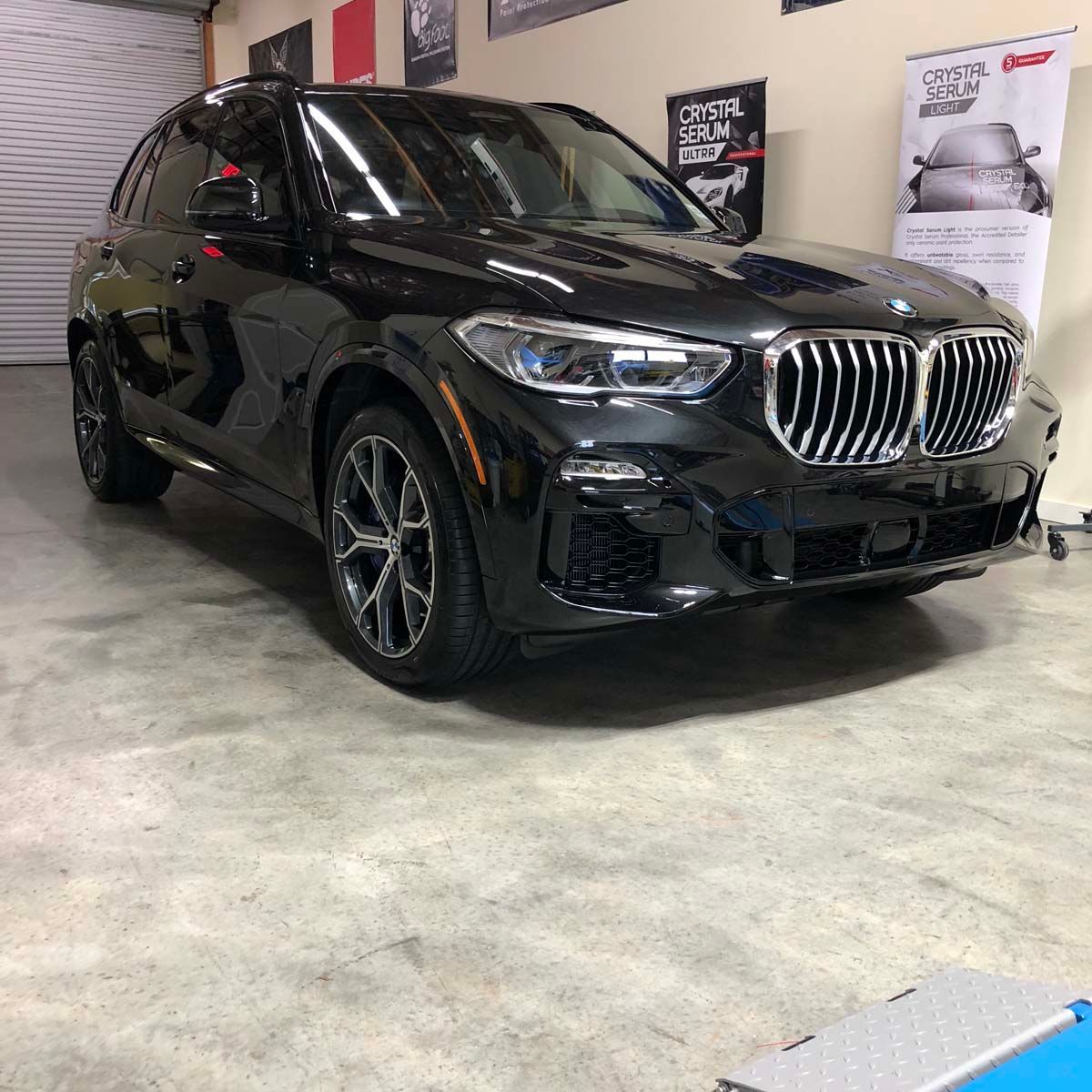 Black BMW X5 SUV parked inside a garage, next to promotional banners.