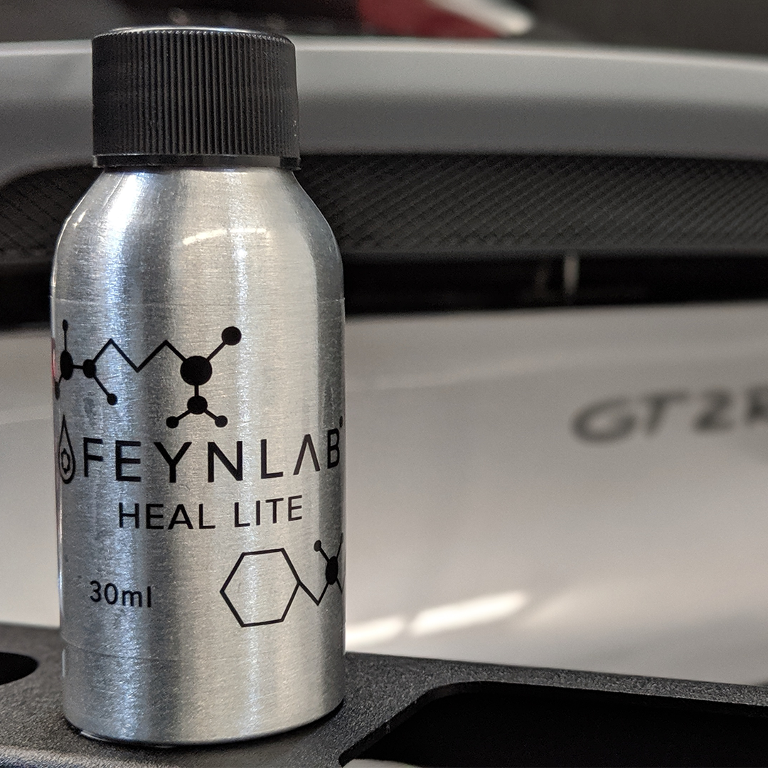 Silver bottle of Feynlab Heal Lite detailing product, with a car in the blurred background.