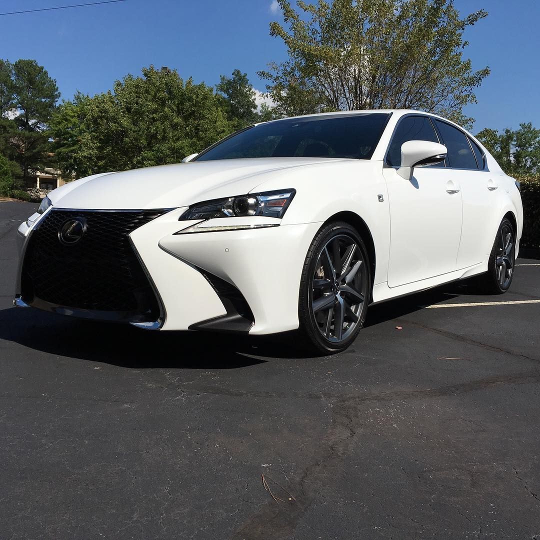 White Lexus sedan parked on asphalt. Black grille and wheels; blue sky background.