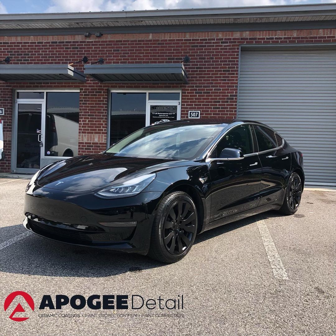Black Tesla Model 3 parked in front of a brick building with garage doors.