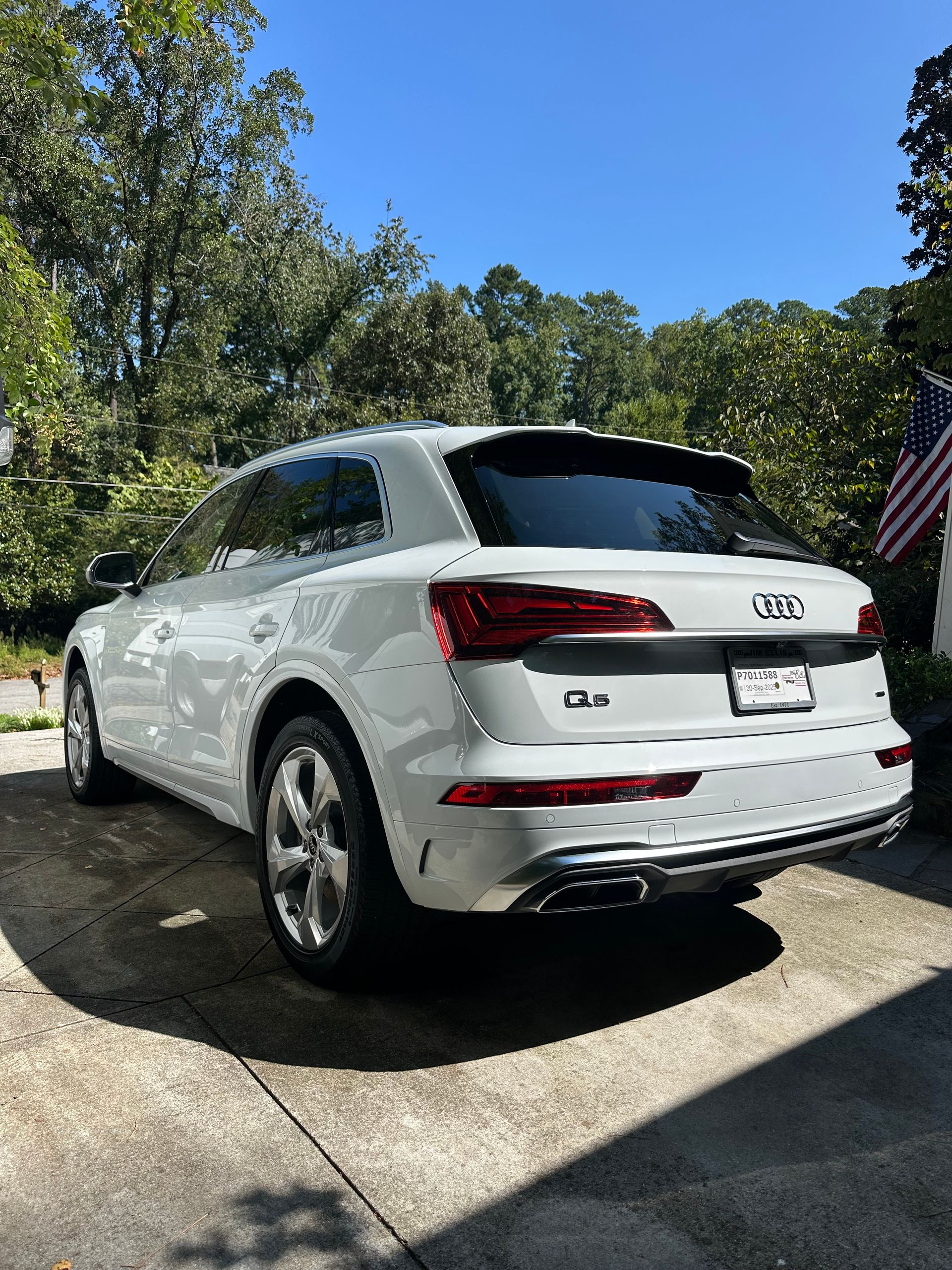 White Audi Q5 SUV parked on a driveway, trees in the background, sunny day.