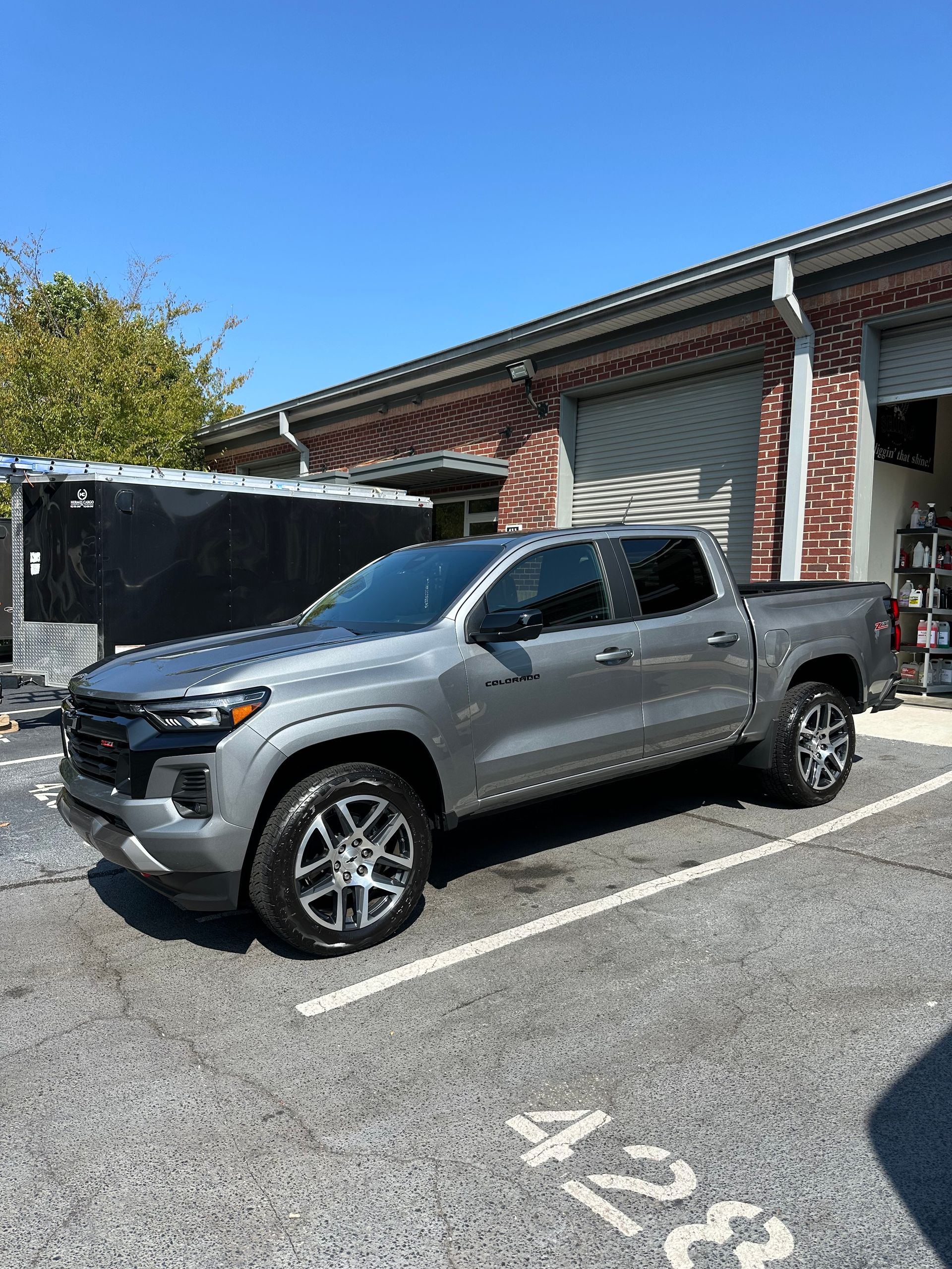 Gray Chevrolet Colorado truck parked on asphalt. Building and clear sky in the background.