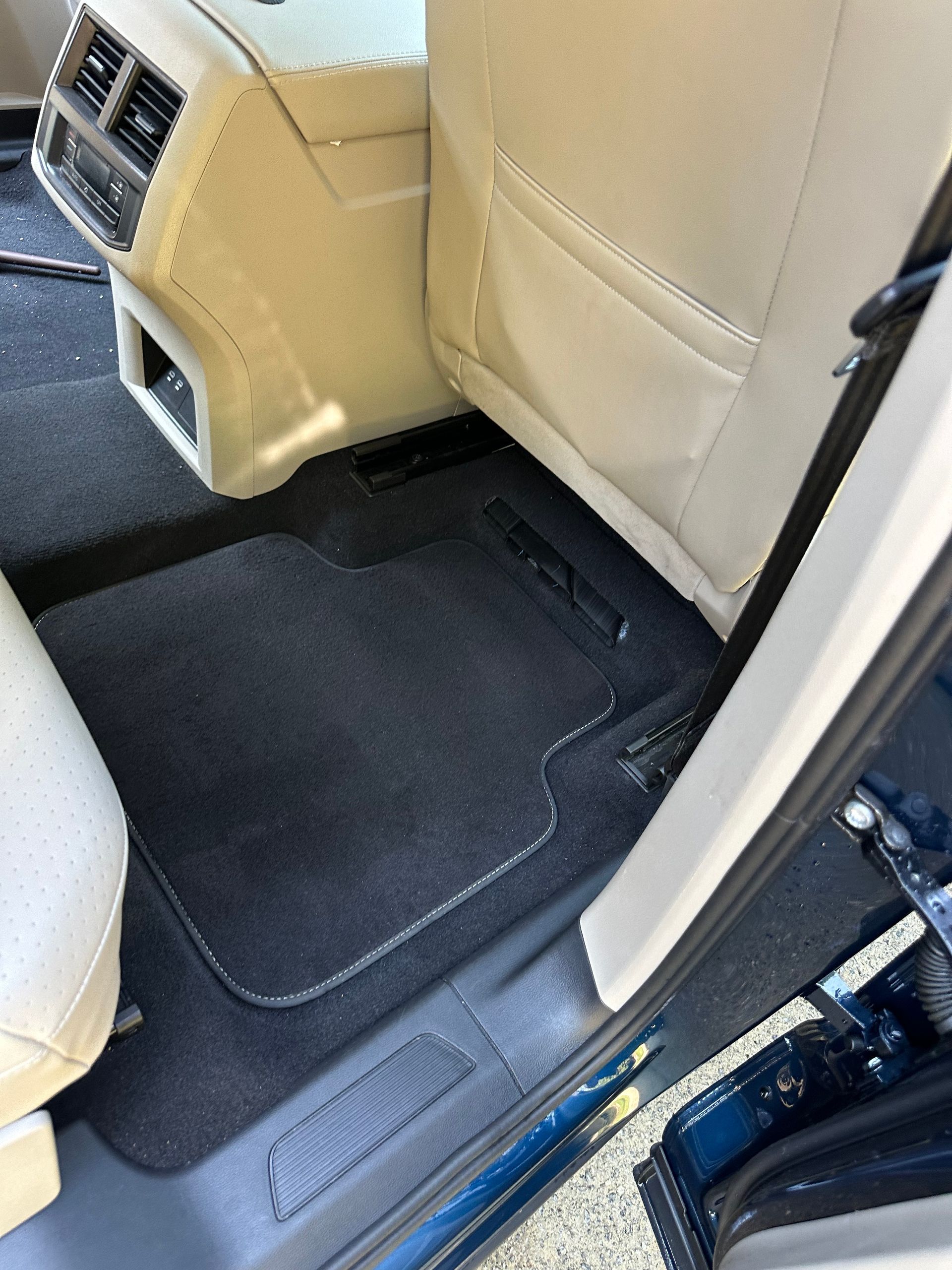Interior car view; black floor mat, beige seats, dark blue door frame.