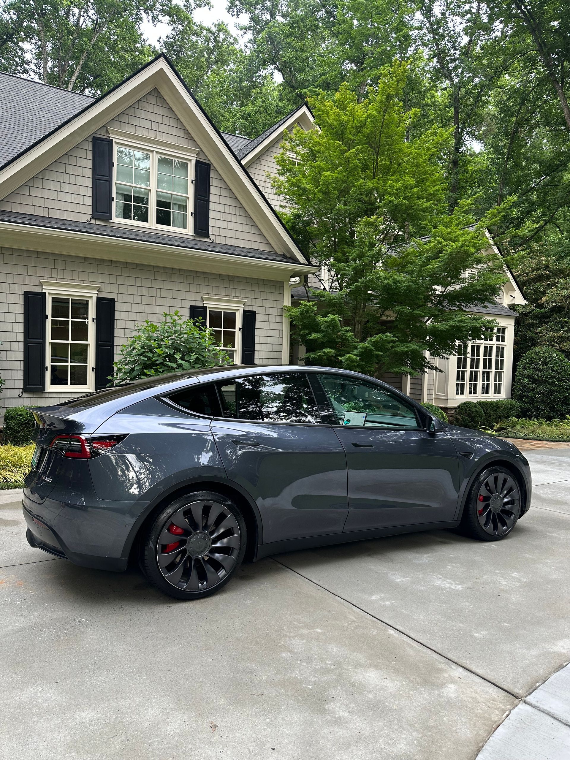 Gray Tesla Model Y parked in front of a light-colored house with black shutters.