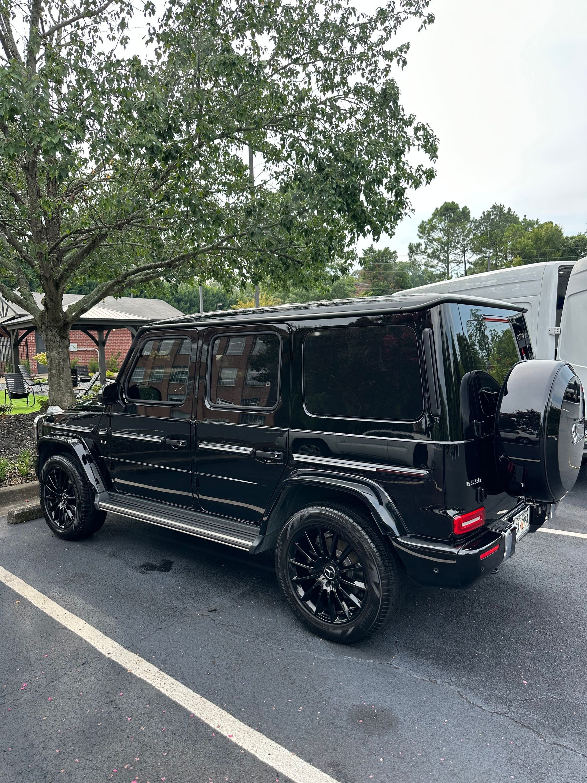 Black Mercedes-Benz G-Class SUV parked outdoors, with black wheels and tinted windows, under a tree.