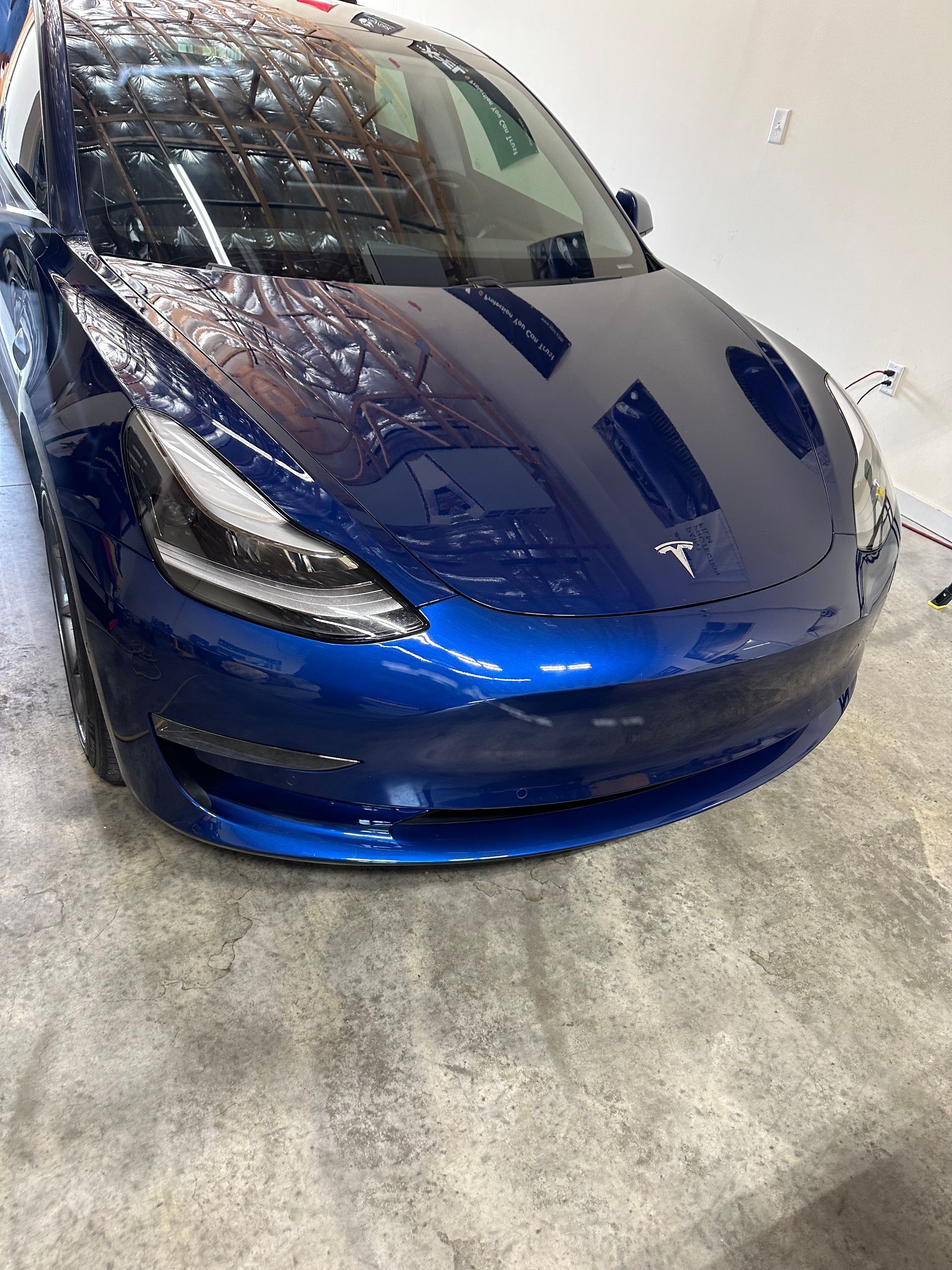 Blue Tesla car, front view, in a bright setting, with wet appearance.