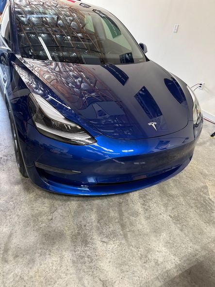 Blue Tesla car, front view, in a bright setting, with wet appearance.
