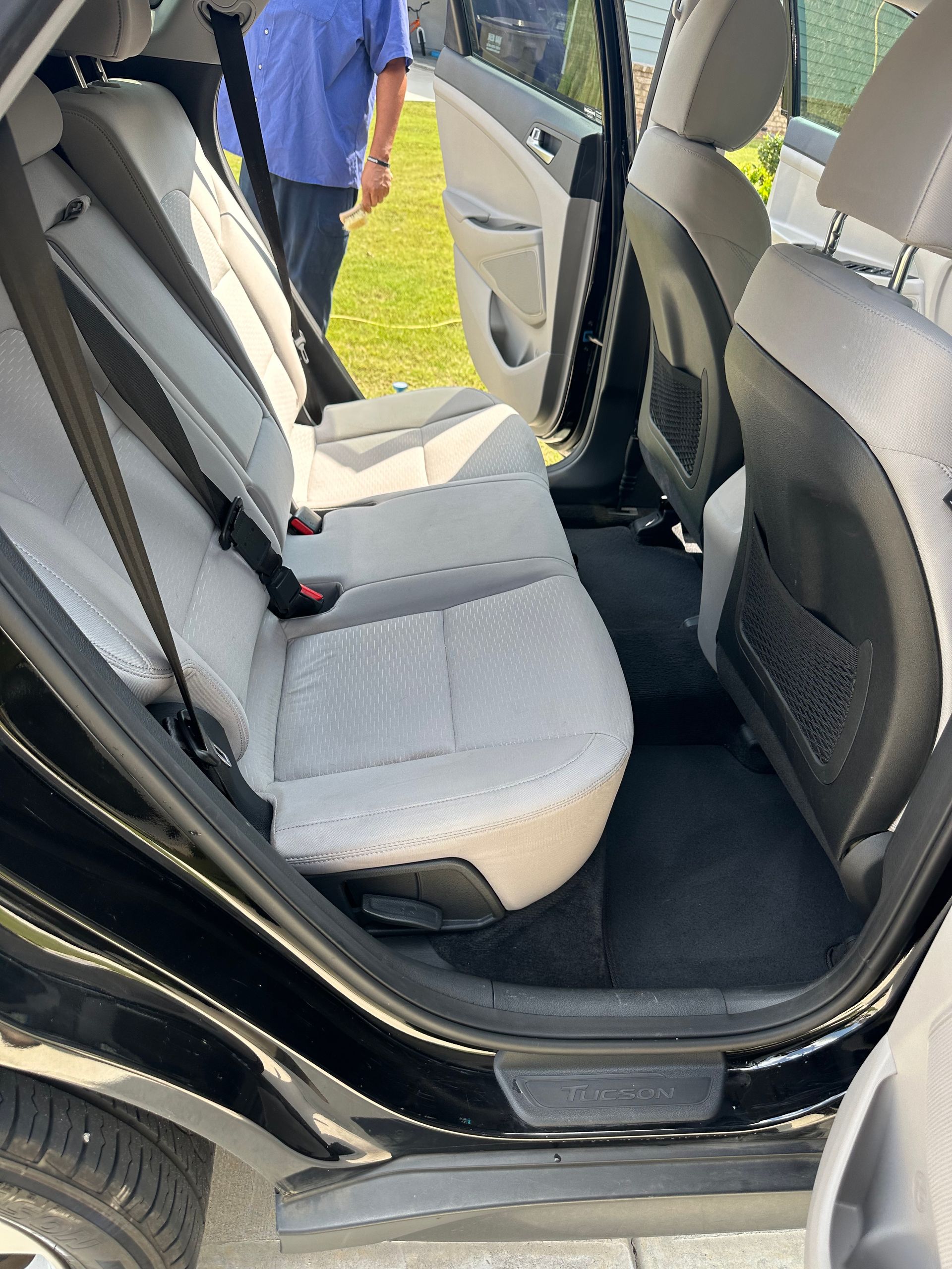 Black car interior with open back door, showing light gray seats, black carpet.