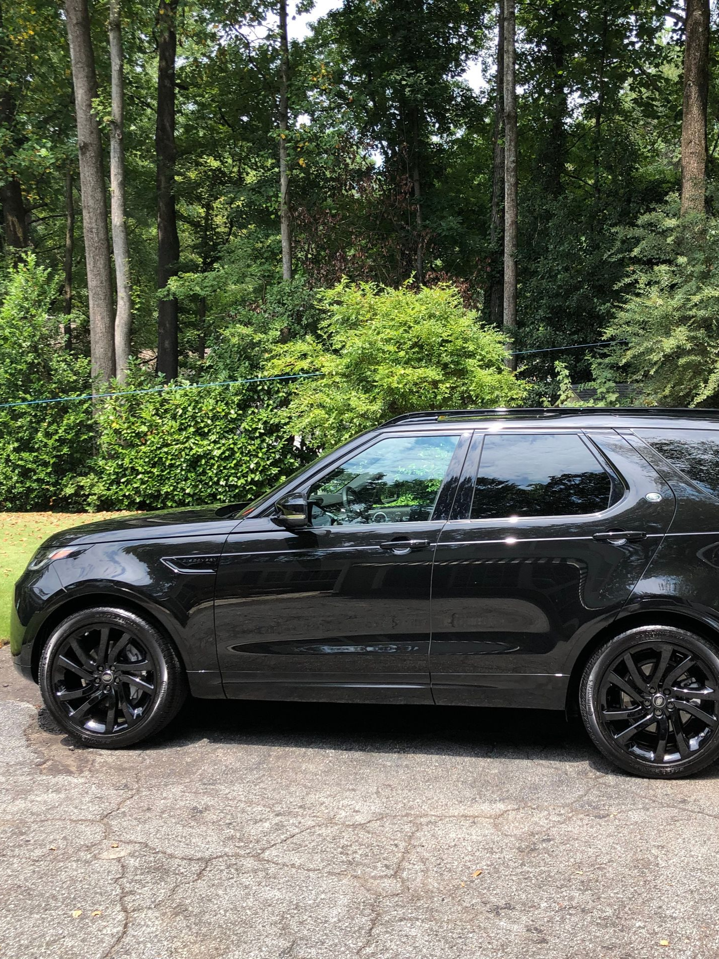 Black Land Rover Discovery SUV parked on a paved driveway in front of trees.