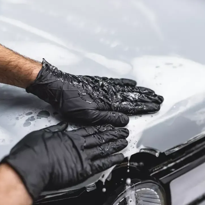 Hands in black gloves applying liquid to a car's hood, likely washing or detailing it.