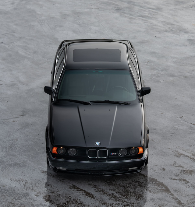 Black BMW sedan, top-down view, parked on a wet, gray surface with a sunroof.