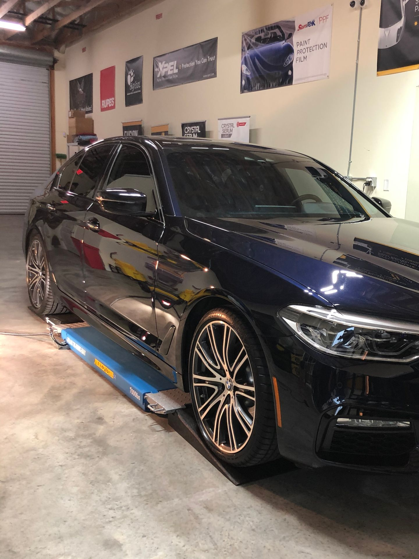 Dark blue BMW sedan on a lift in a garage, with posters on the wall.