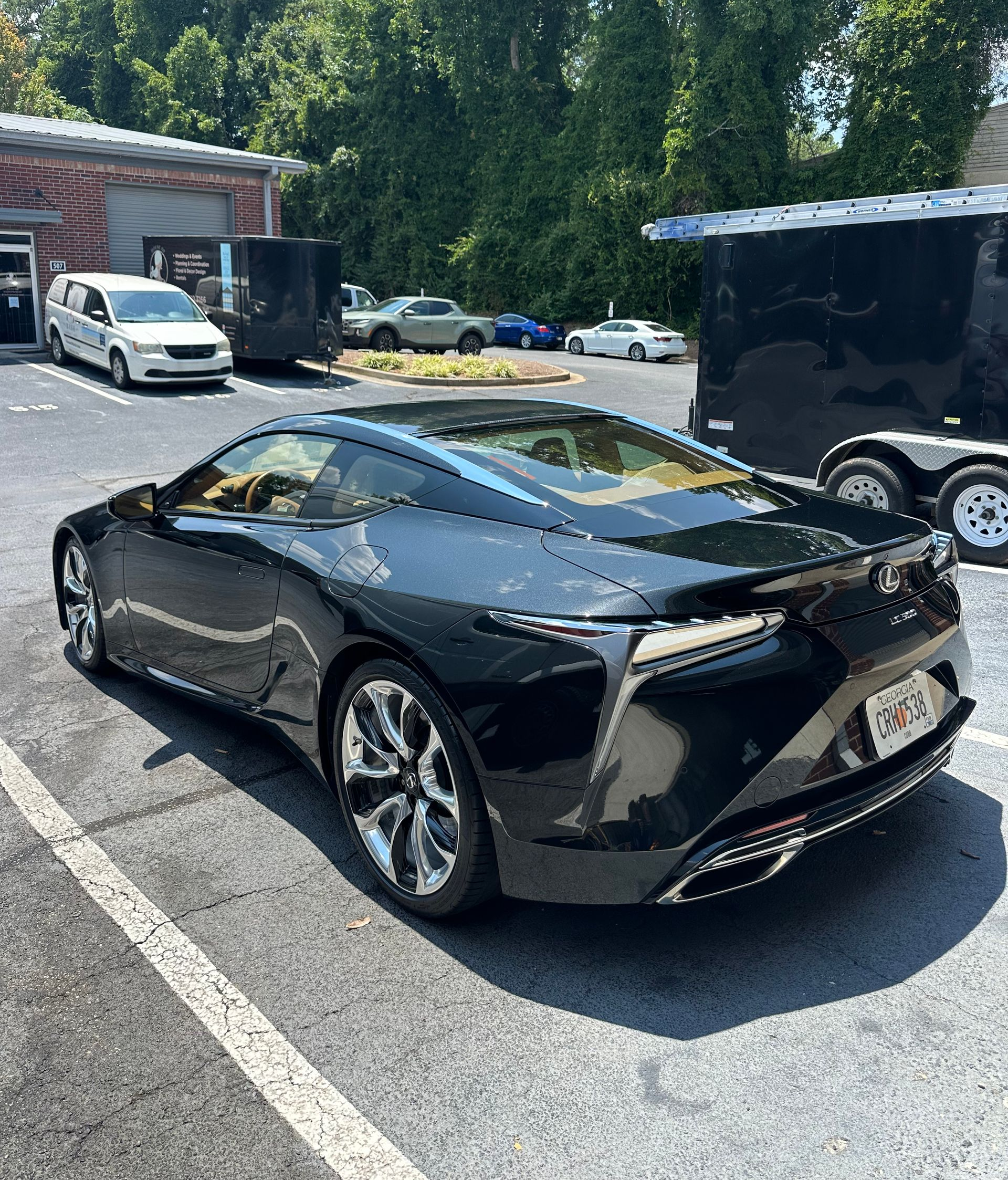 Black Lexus LC 500 coupe parked outside a building on an asphalt surface; other vehicles visible.