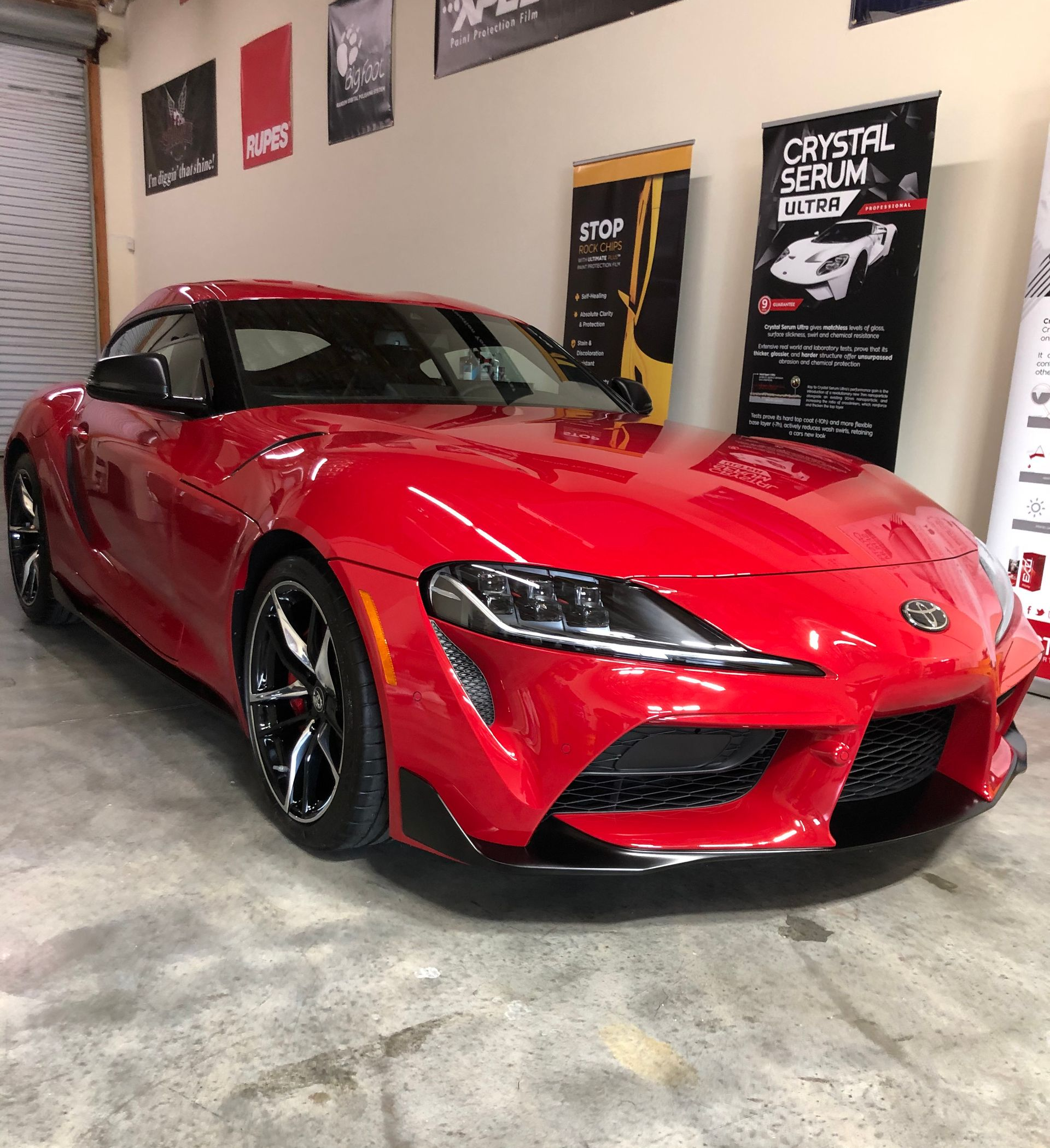 Red Toyota Supra sports car parked in a garage with promotional banners in the background.