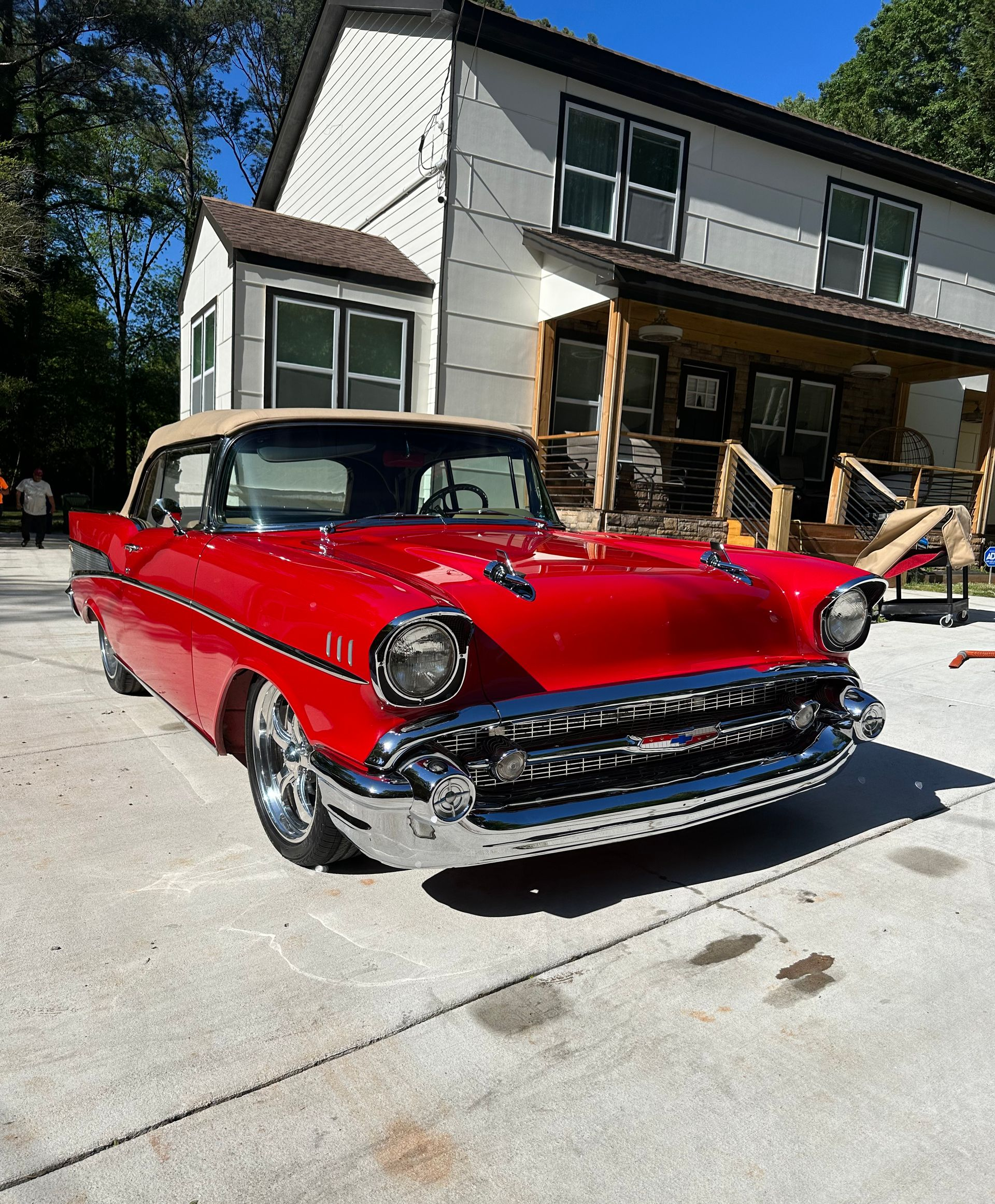 Red classic car parked in front of a white house with a porch.