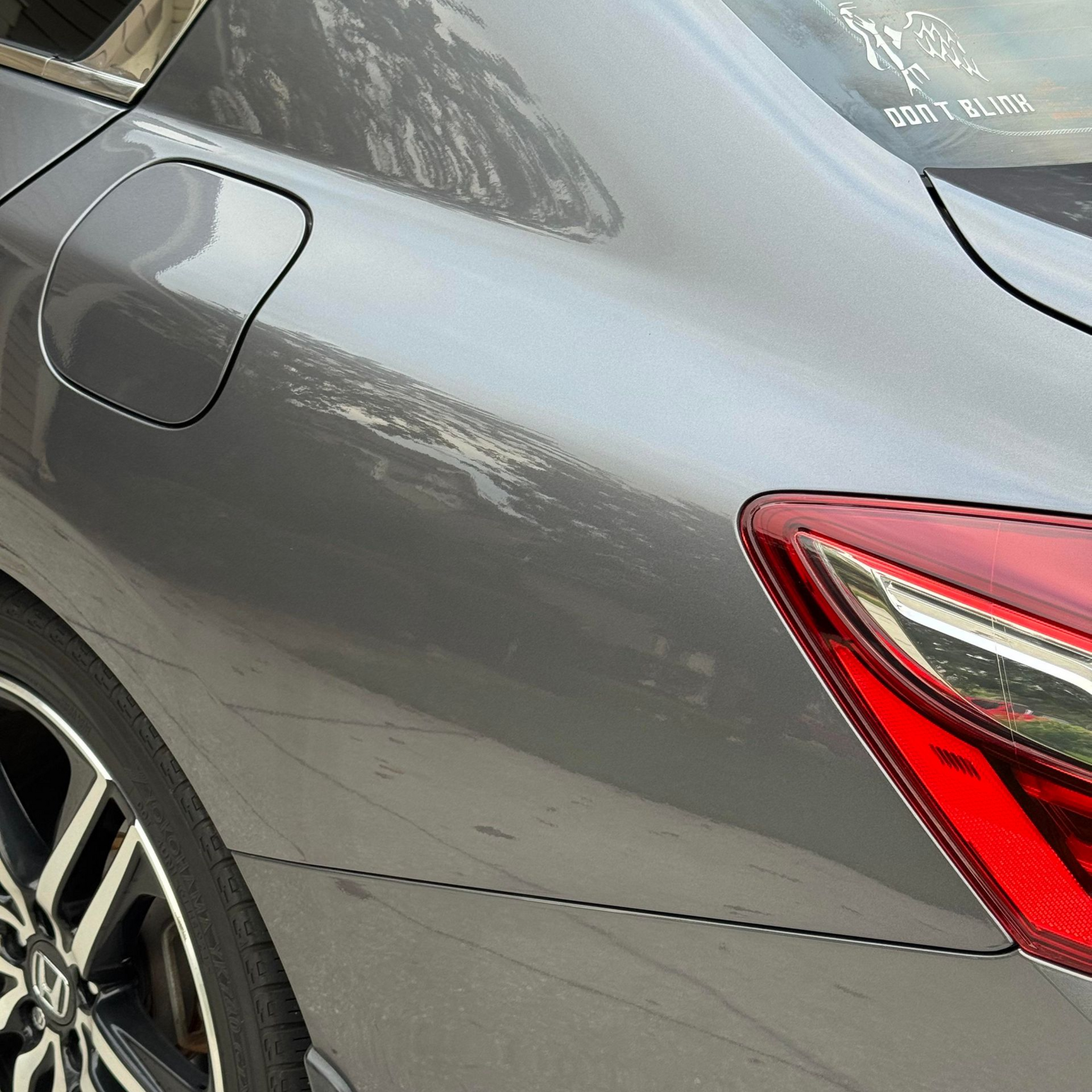 Gray car's rear side with a taillight, gas cap door, and a partially visible black wheel.