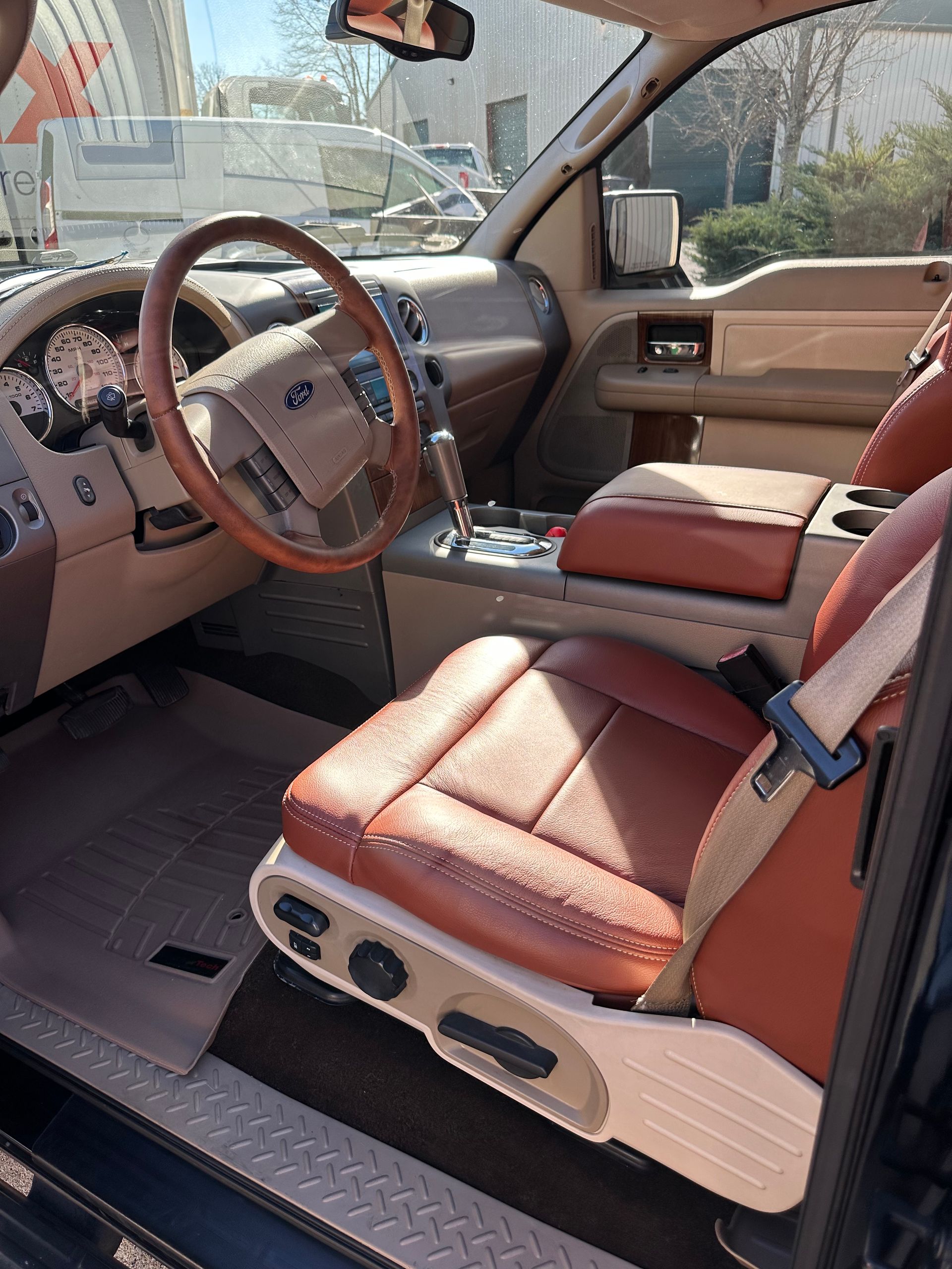 Interior of a Ford F-150 truck with tan and brown leather seats, wooden steering wheel, and tan dashboard.