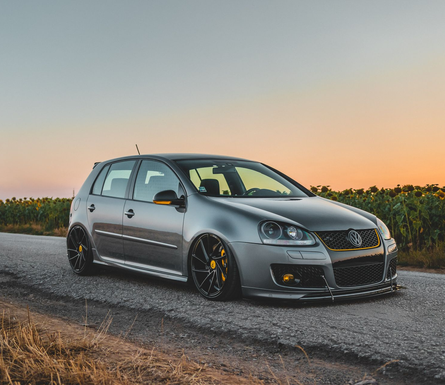 Gray Volkswagen Golf on a road, lowered with black and yellow rims, daytime.