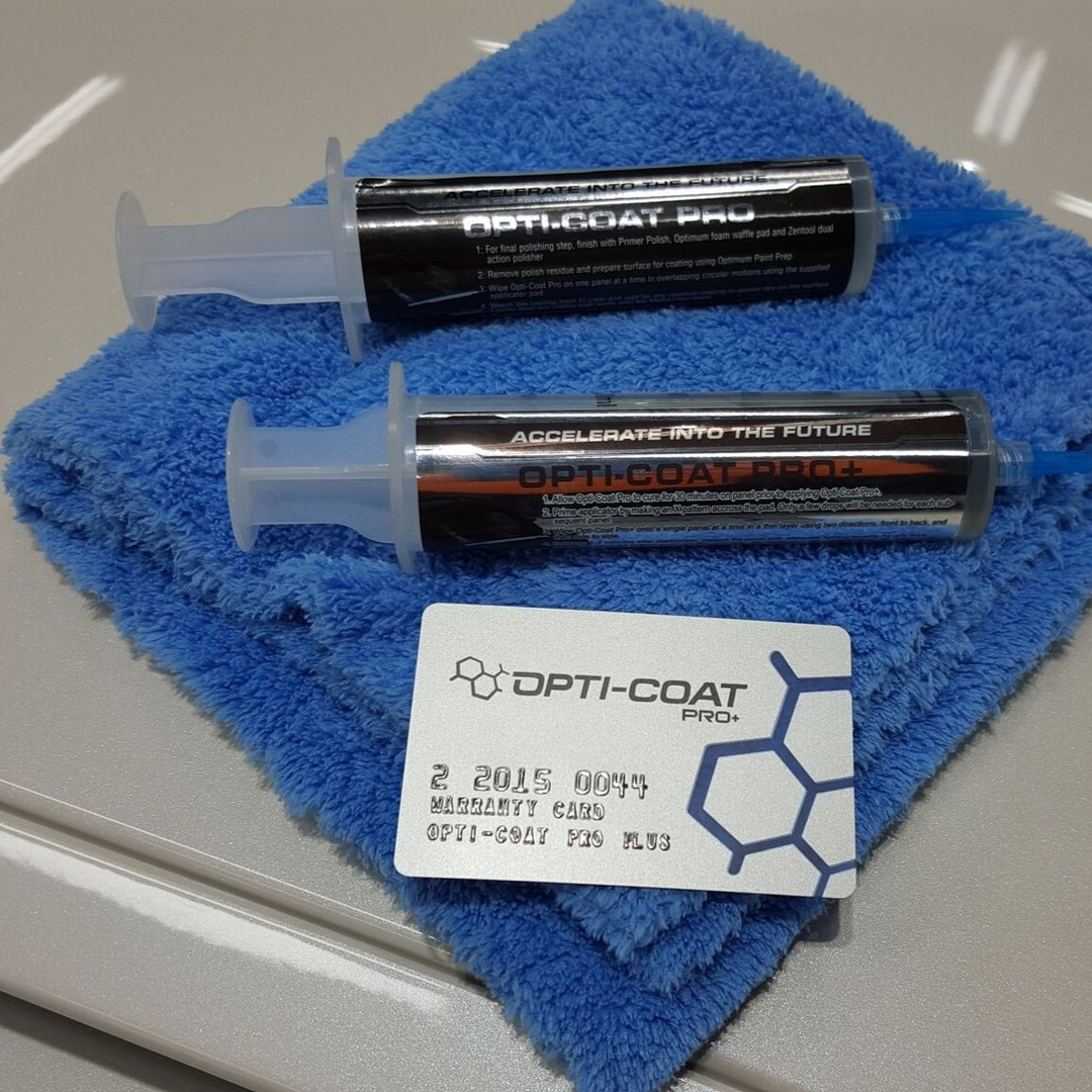 Two Opti-Coat Pro+ syringes on a blue microfiber cloth, with a product information card.