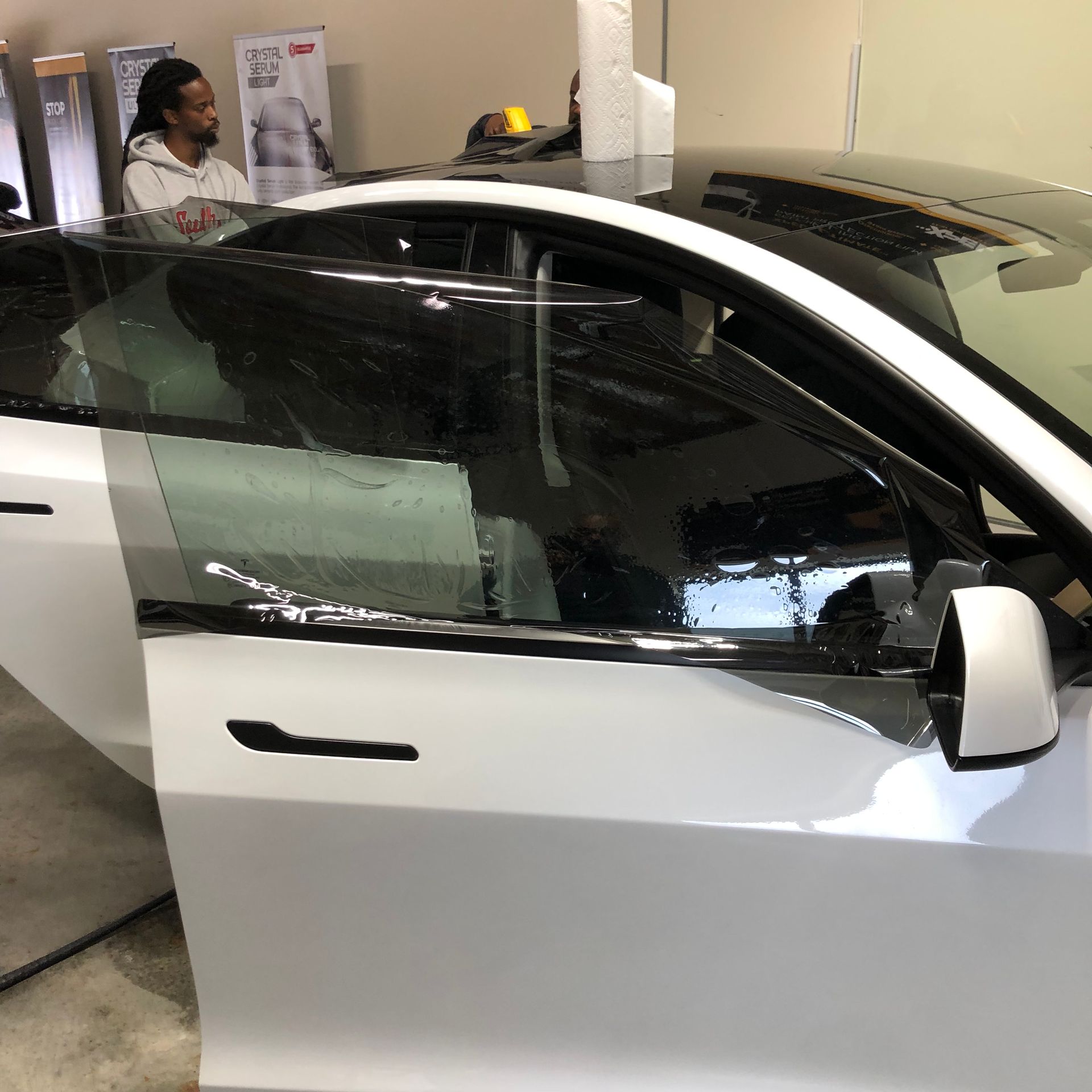 A person applying window tint to a white car in a garage.