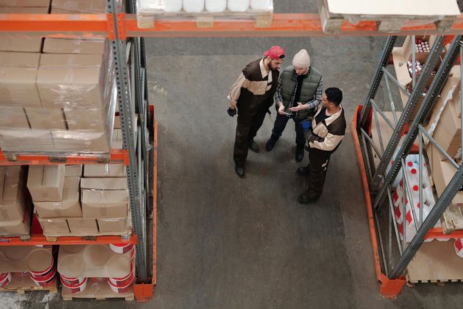 Three people in a warehouse looking at a tablet near shelves of boxes.