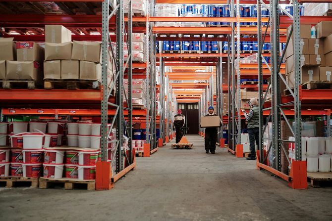 Warehouse interior with tall metal shelving filled with goods, and workers moving boxes.