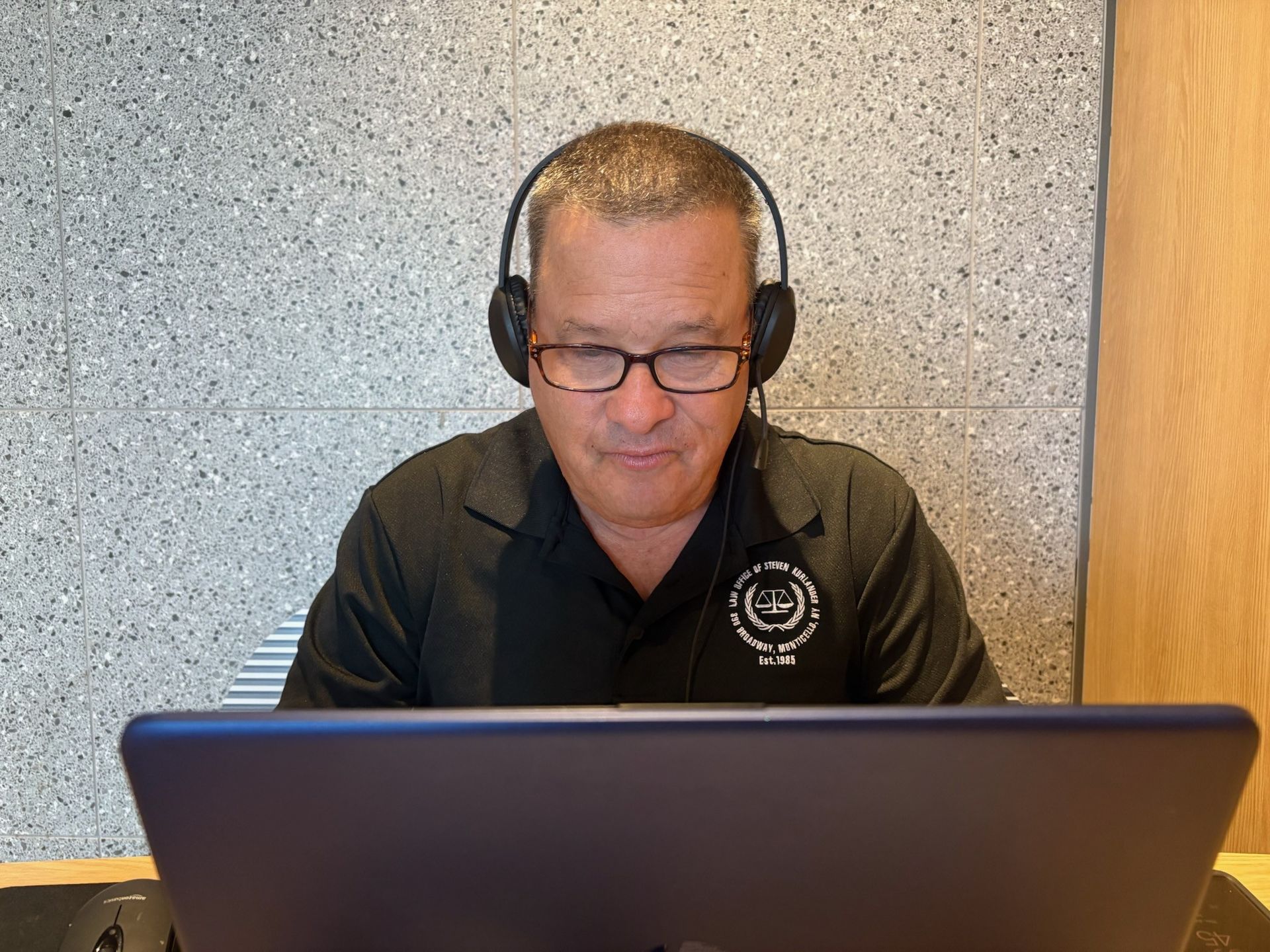 Man wearing glasses and headphones working on a laptop in front of a speckled wall. Man wearing glasses and headphones working on a laptop in front of a speckled wall.
