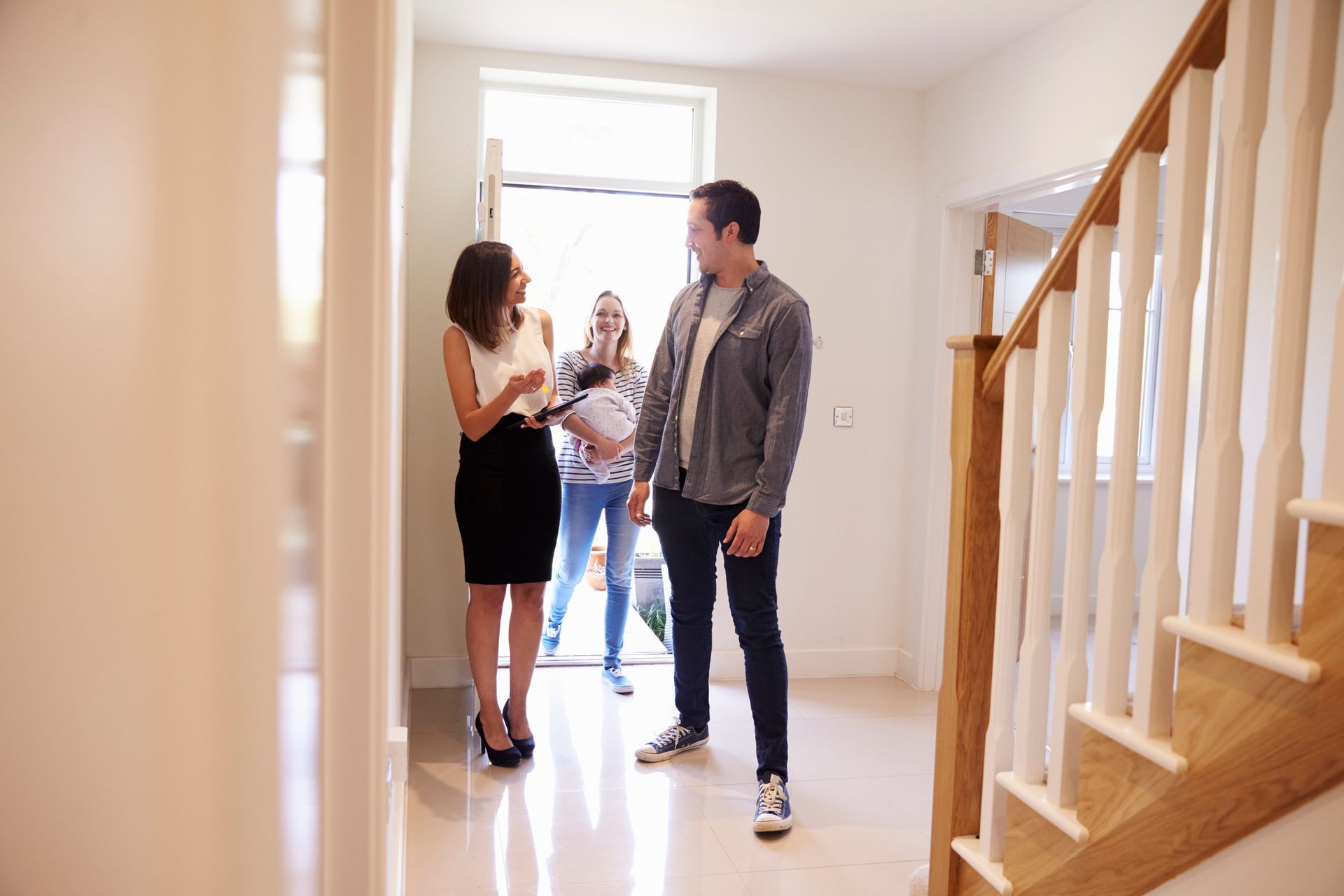 Real estate agent showing house to a couple; entrance doorway, staircase visible.